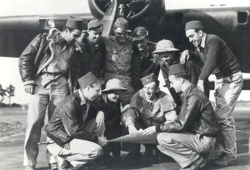black and white photo of young men in front of a bomber looking at a map